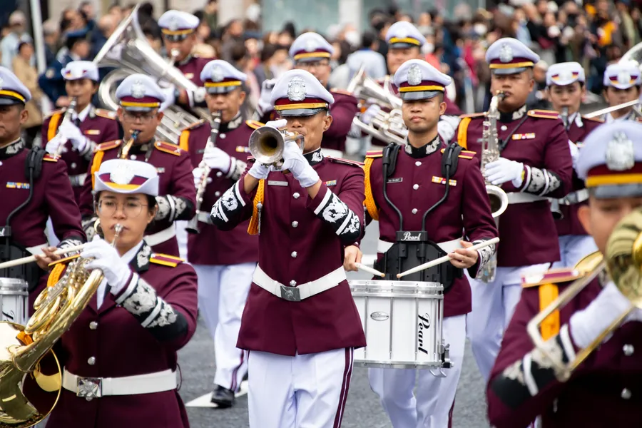 えんじ色の制服で演奏しながら行進する警察音楽隊（過去の様子）
