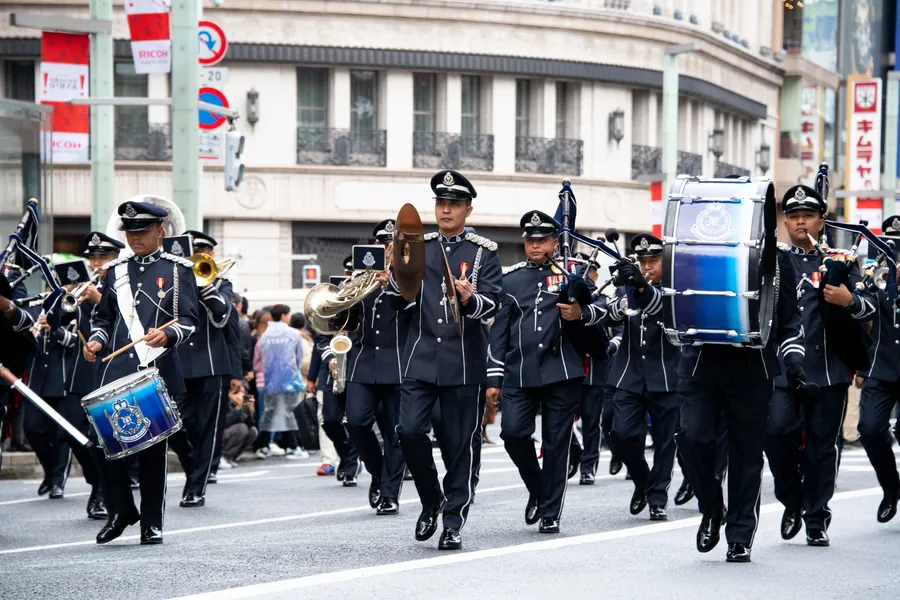 紺色の制服でバグパイプやドラムを演奏しながら行進する警察音楽隊（過去の様子）